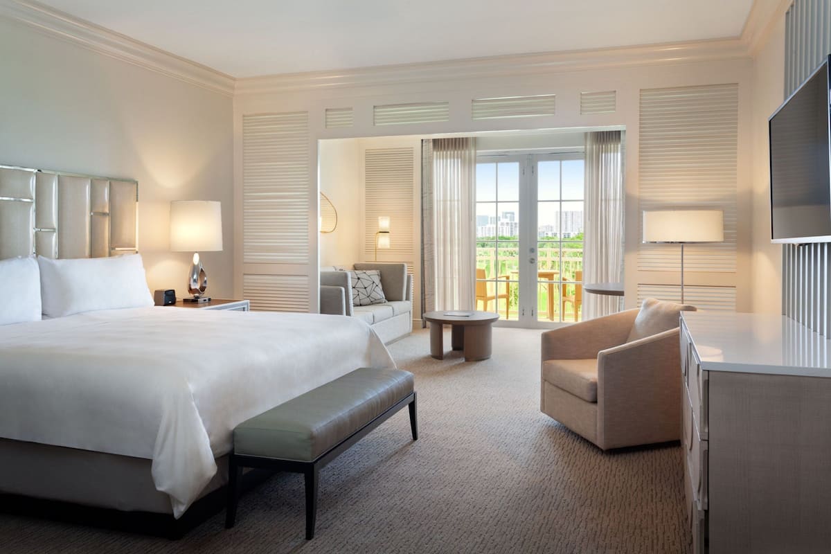 A hotel room with a large bed, a sofa, a chair, a desk, and a TV.