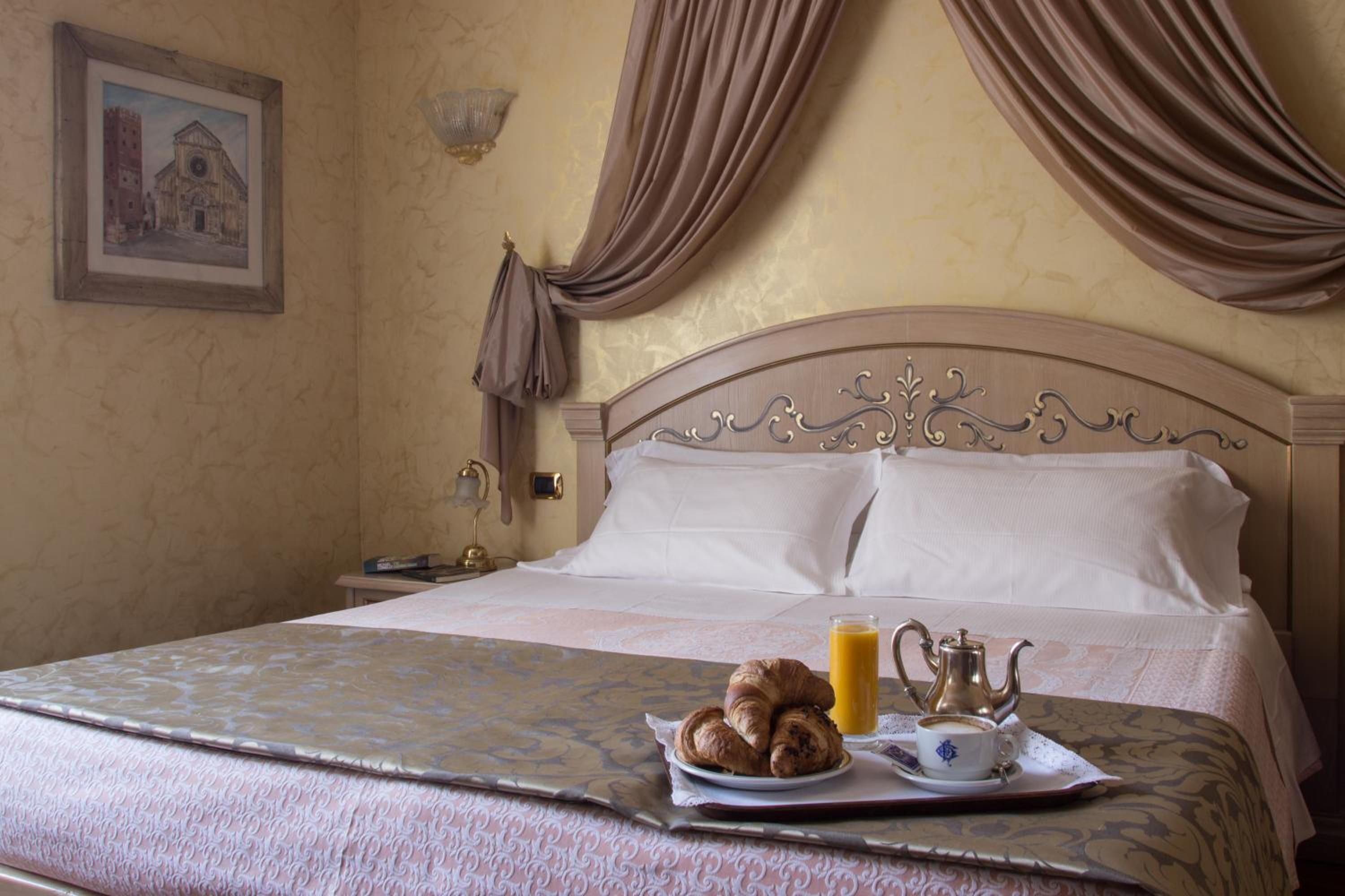 A hotel room with a bed, a painting on the wall, and a breakfast tray with croissants and coffee.