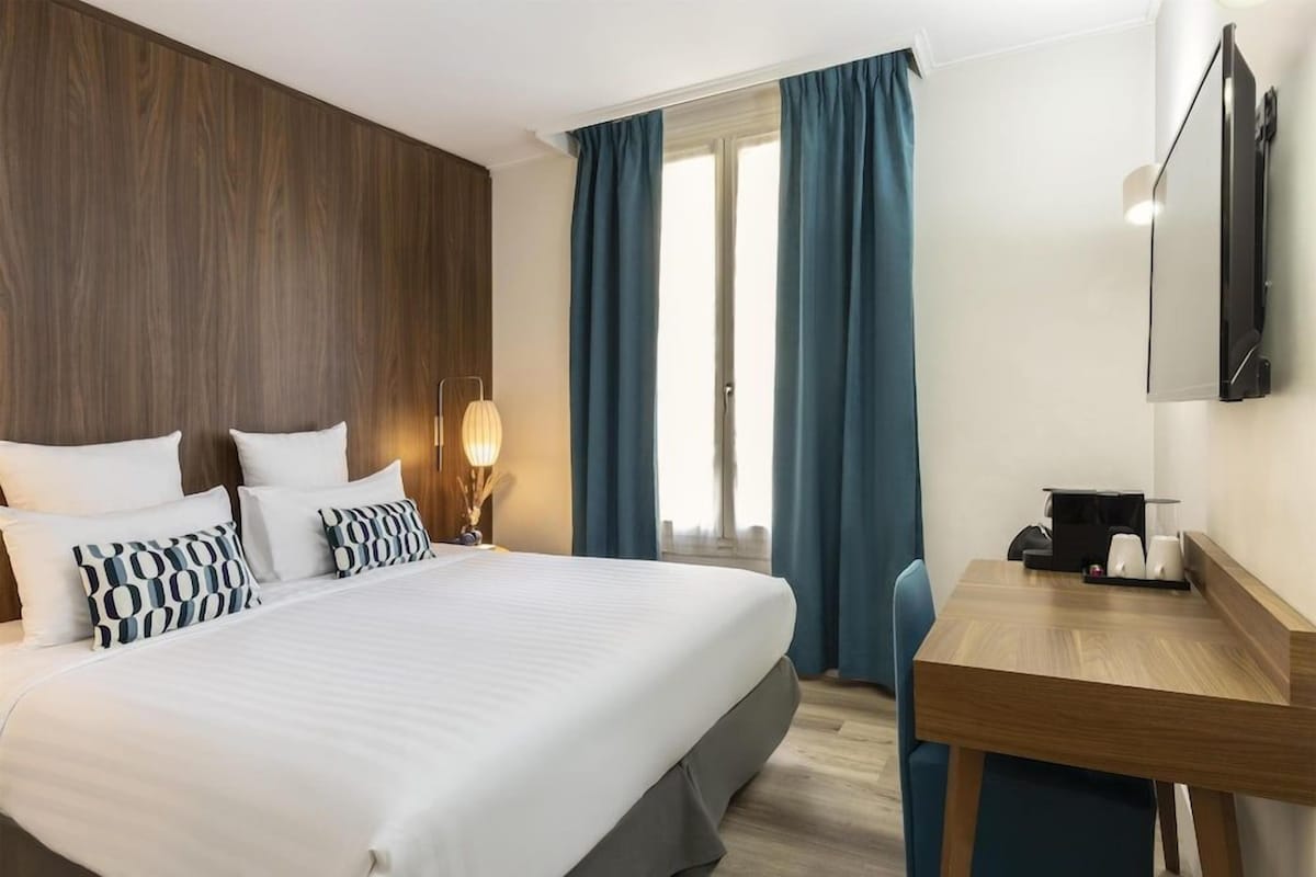 A hotel room with a large bed, a desk, and a television.
