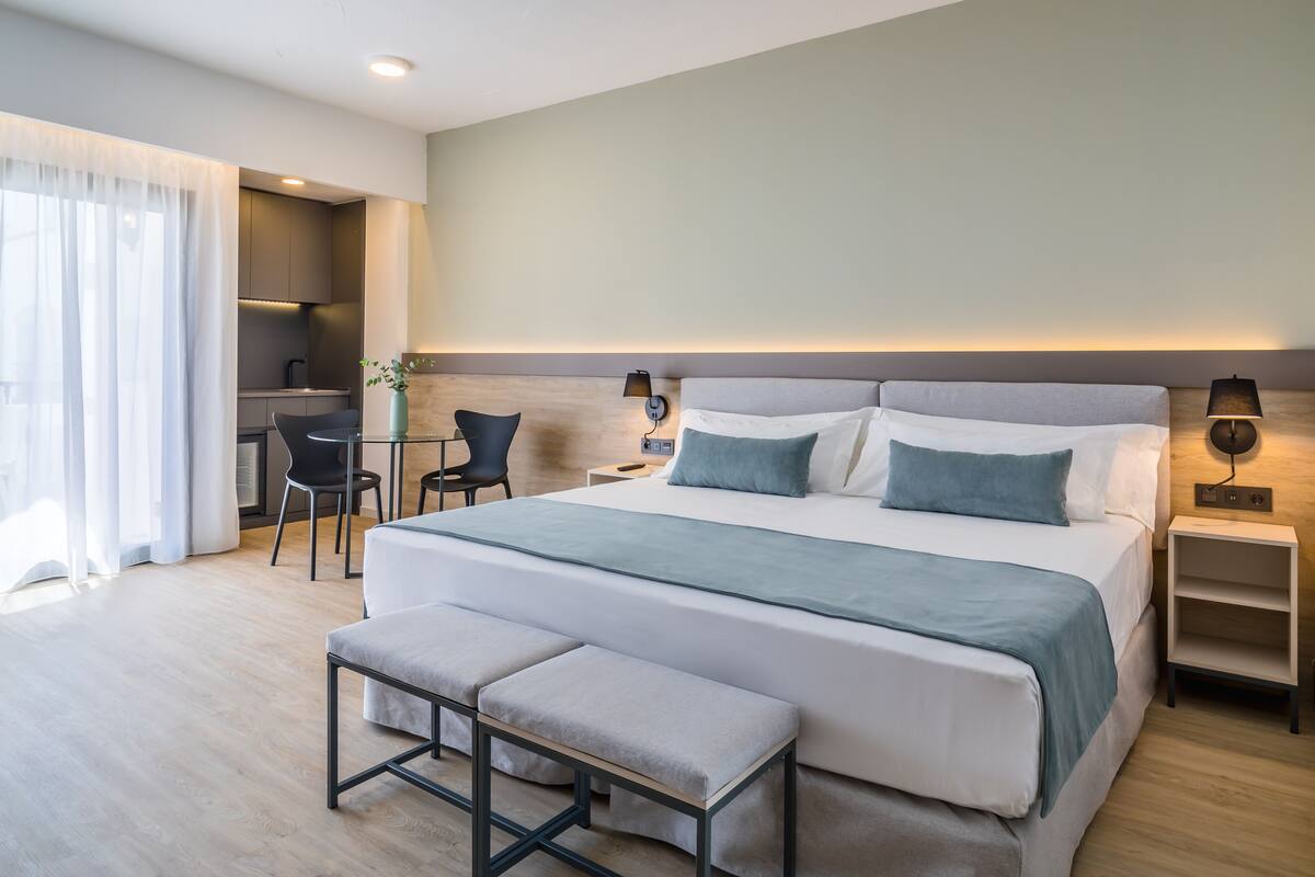Una habitación de hotel moderna con una cama grande, un escritorio, una silla y un banco.