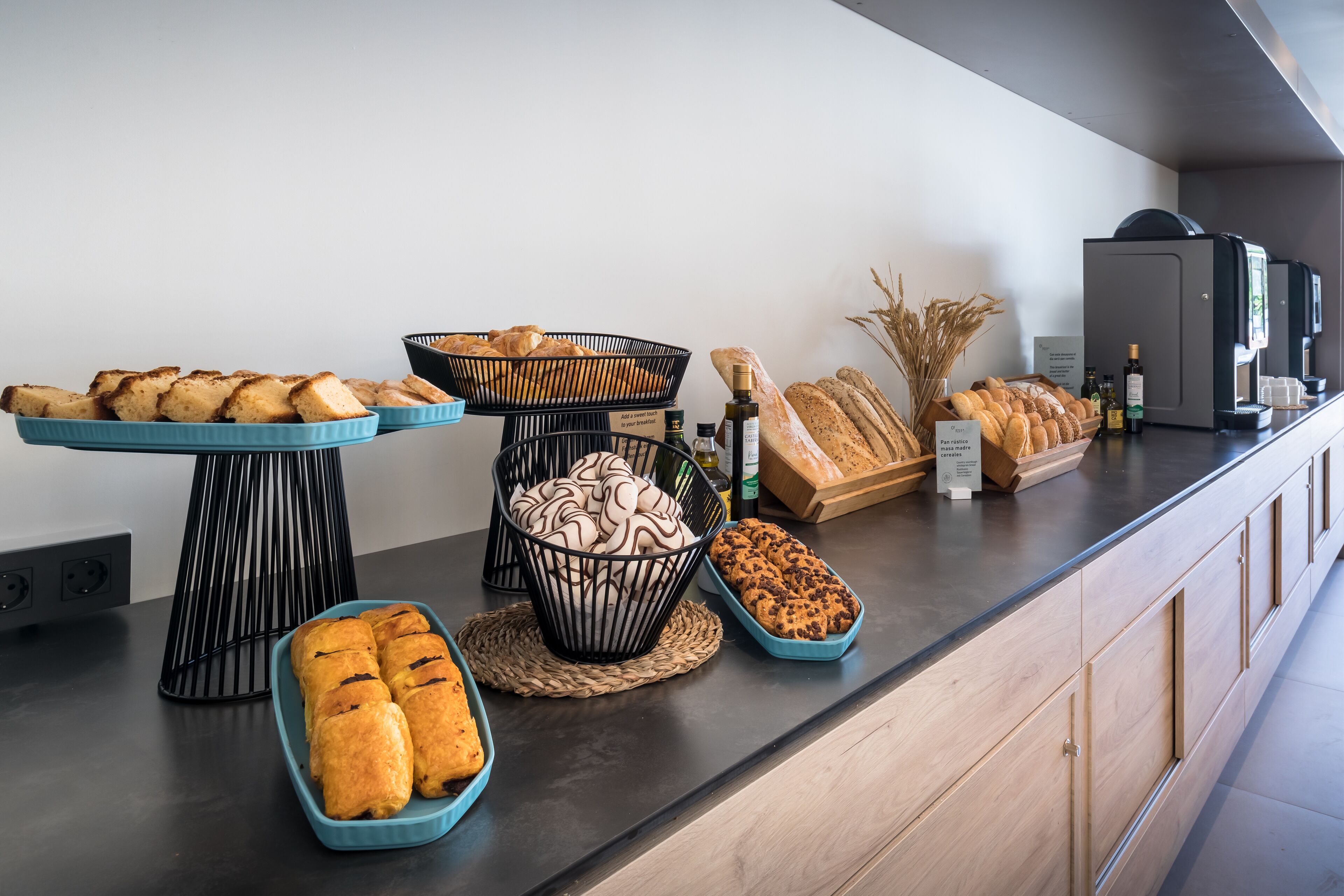 A buffet counter with various baked goods, including bread and pastries, arranged on a modern counter with a neutral color scheme.
