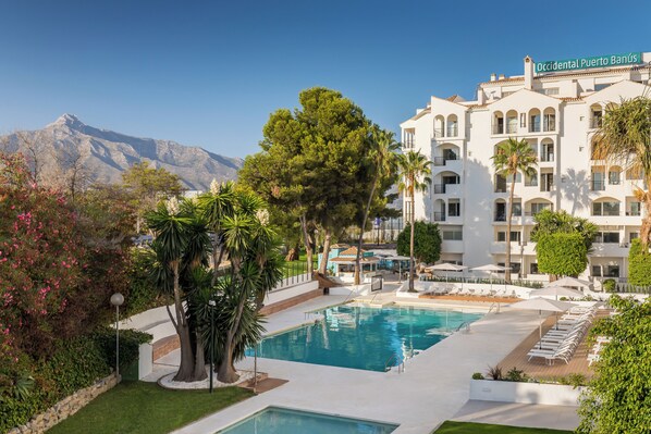 A hotel with a pool, surrounded by greenery and palm trees, with a mountain in the background. - Occidental Puerto Banus (Marbella)