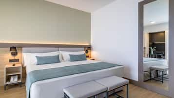 A modern hotel room with a large bed, bedside tables, a bench, and a mirror reflecting the room.