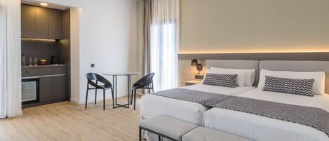 A modern hotel room with a large bed, a small desk, and a kitchenette.