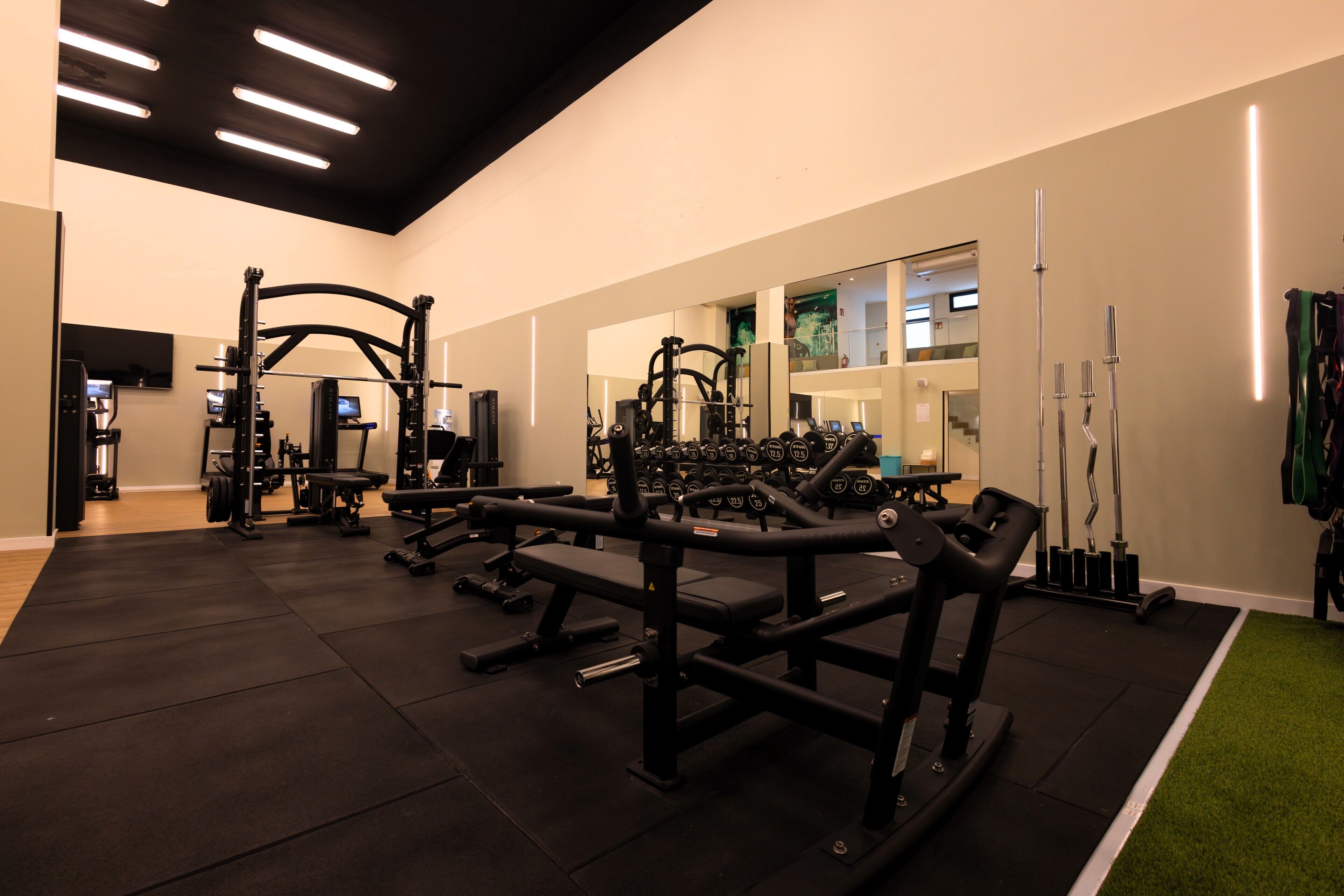 Un gimnasio con diversos equipos de ejercicio, incluyendo bancos, máquinas de pesas y pesas sueltas.