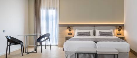 Una habitación de hotel moderna con una cama grande, mesitas de noche, una mesa de vidrio con sillas y un banco.