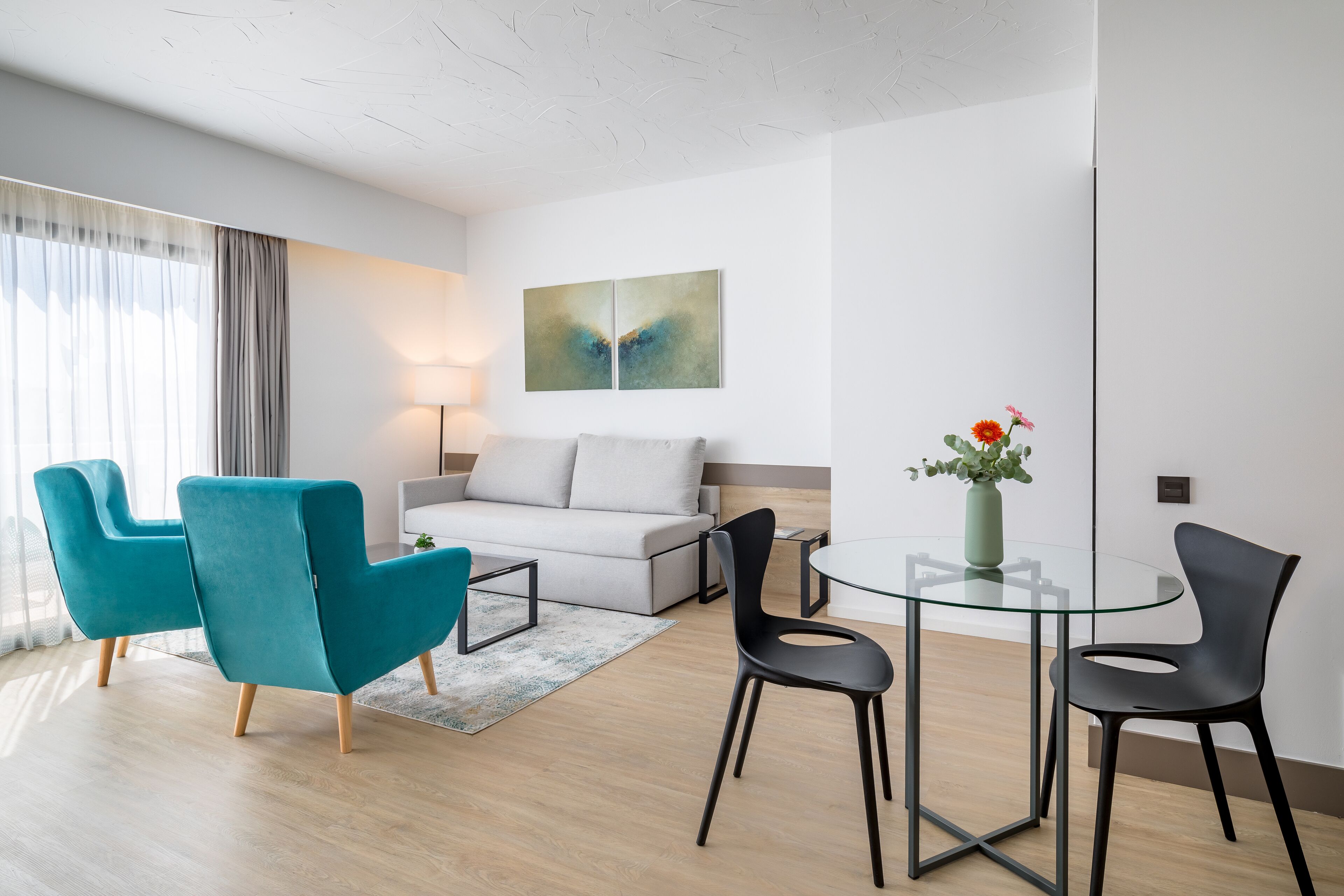 Uma sala de estar moderna com um sofá, duas poltronas verde-água, uma mesa de vidro e uma mesinha de centro.