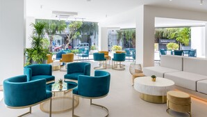 A modern lounge area with teal and gold furniture, a white sofa, and a view of the street.