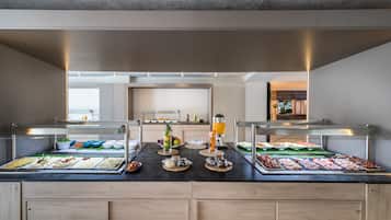 Een buffet met diverse etenswaren en drankjes, een keuken in de achtergrond en een modern interieur.