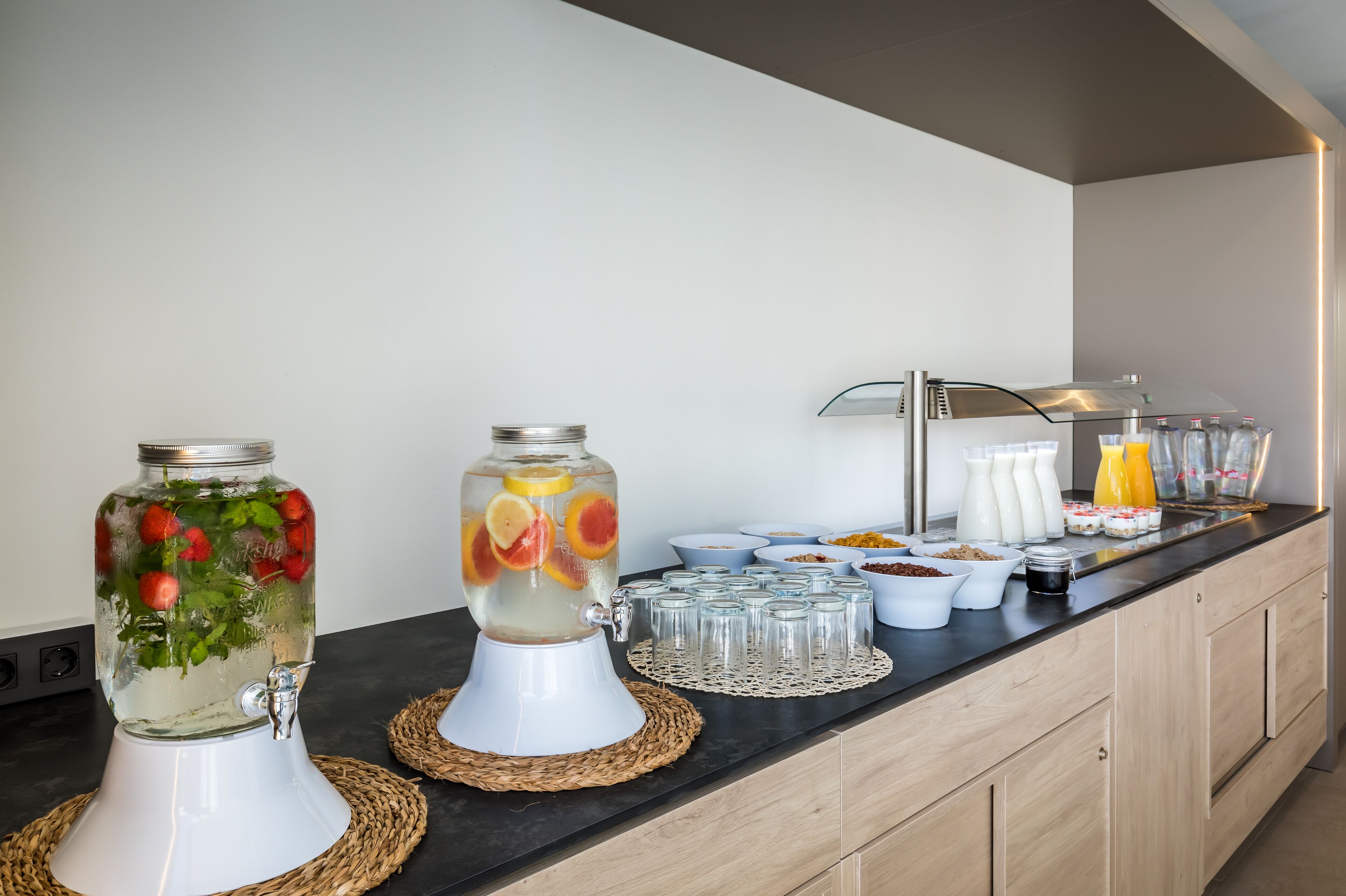 A breakfast bar with a fruit-infused water dispenser, a juice dispenser, and various breakfast items.