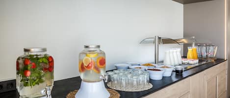 A breakfast bar with a fruit-infused water dispenser, a juice dispenser, and various breakfast items.