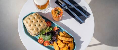 A meal consisting of a sandwich, fries, salad, and a small bowl of sauce, served on a white plate with a fork and knife set on a napkin.