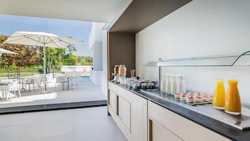 Un bar où l’on sert le petit-déjeuner, avec un choix varié de plats et de boissons, des places assises à l’extérieur, protégées par des parasols, et une vue sur la verdure.