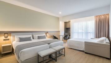 Ein Hotelzimmer mit einem großen Bett, einem kleineren Bett, einem Sofa, einem Schreibtisch und einem Fenster mit Vorhängen.