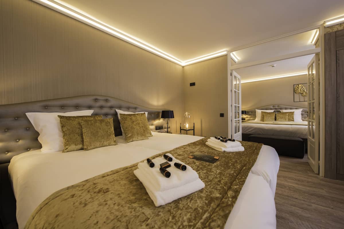 A hotel room with a large bed, a bedside table with a lamp, and a mirror reflecting the room.