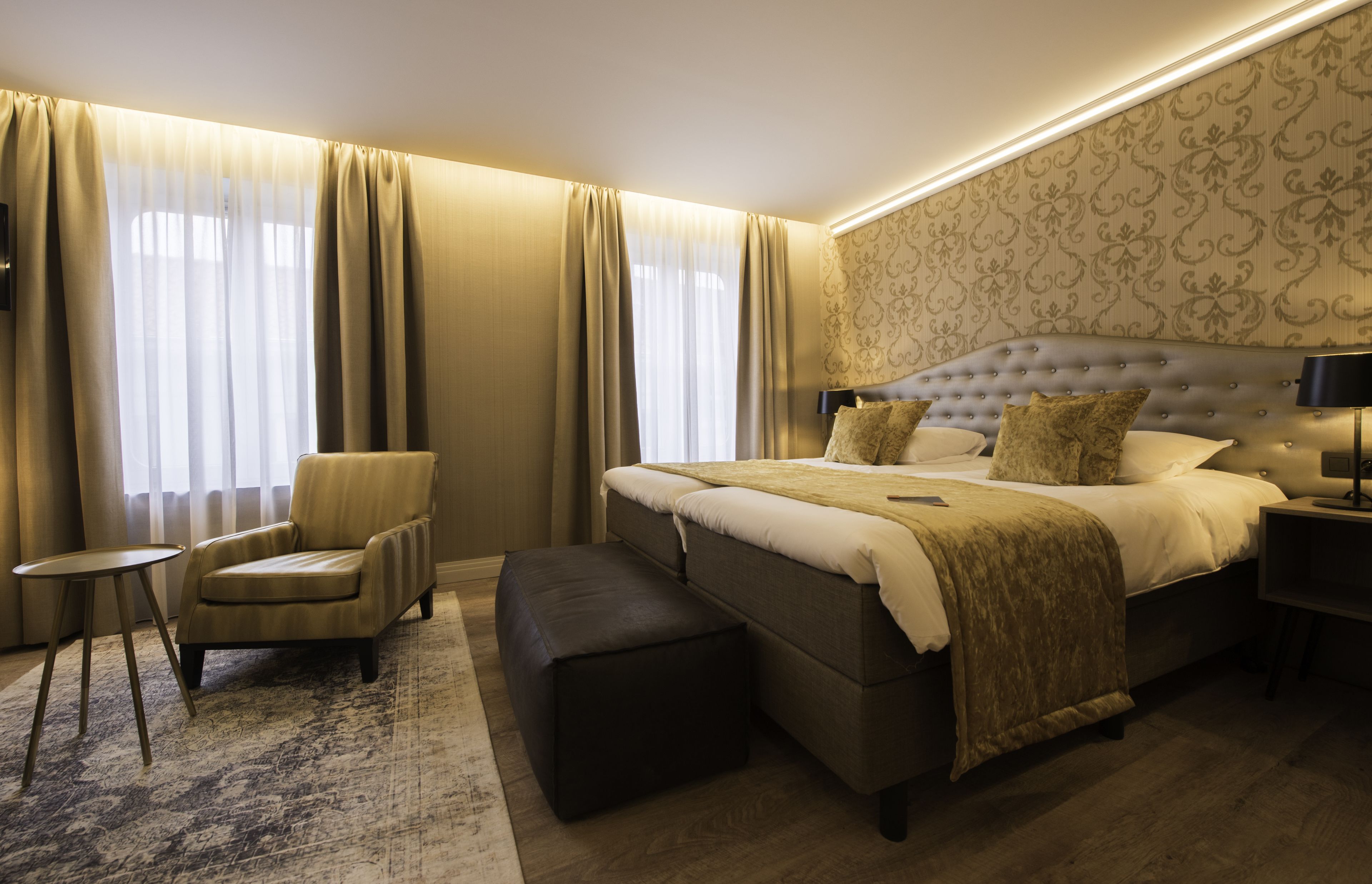 Een ruime slaapkamer met een groot bed, een stoel, een tafeltje en een bankje.