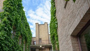 An outdoor seating area with wicker furniture, a covered patio, and a view of a brick building with a tower. - Hotel Acacia (Bruges)