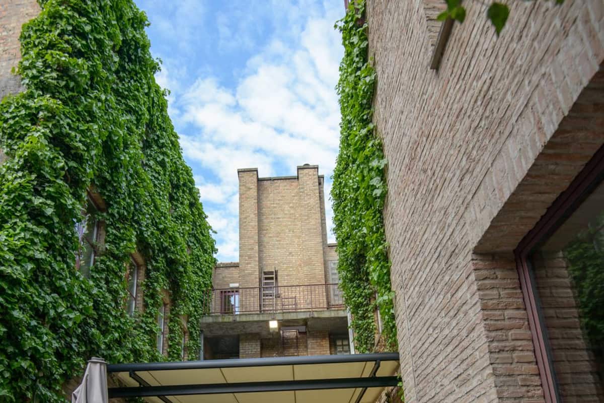 An outdoor seating area with wicker furniture, a covered patio, and a view of a brick building with a tower.