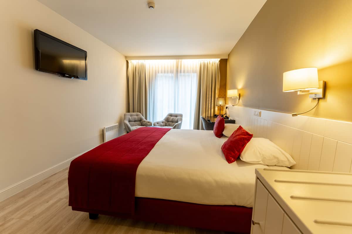 A hotel room with a bed, a television mounted on the wall, a desk, and a chair.