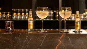 A bar area with two glasses of a clear cocktail, a bottle of tonic water, and a candle holder. - Hotel Acacia (Bruges)