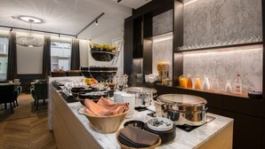 A modern breakfast bar with a marble backsplash, a variety of breakfast items, and a seating area with chairs and a table. - Hotel Acacia (Bruges)