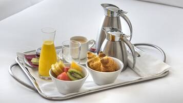 A breakfast tray with croissants, a fruit bowl, a glass of orange juice, a coffee cup, and a silver pitcher.