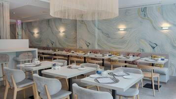 Un comedor moderno con mesas blancas y sillas grises, que presenta una pared de mármol con un diseño en espiral e iluminación colgante.