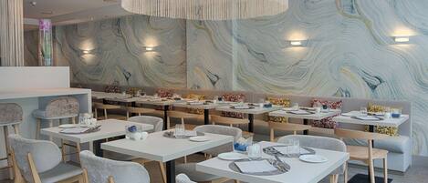A modern dining area with white tables and grey chairs, featuring a marble wall with a swirling pattern and pendant lighting.