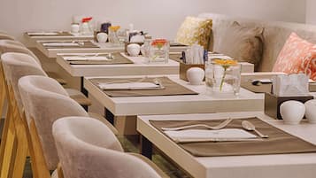 Un comedor con varias mesas dispuestas para el servicio, cada una con un mantel individual, cubiertos y un florero con flores.