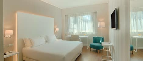 A modern hotel room with a large bed, a desk, a chair, a TV, and a small table.