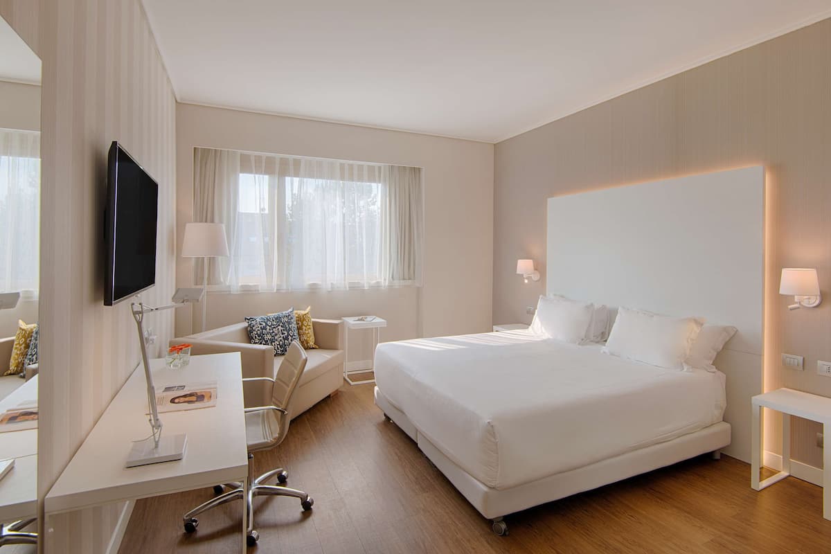 A modern hotel room with a large bed, a desk with a computer, a chair, and a TV mounted on the wall.