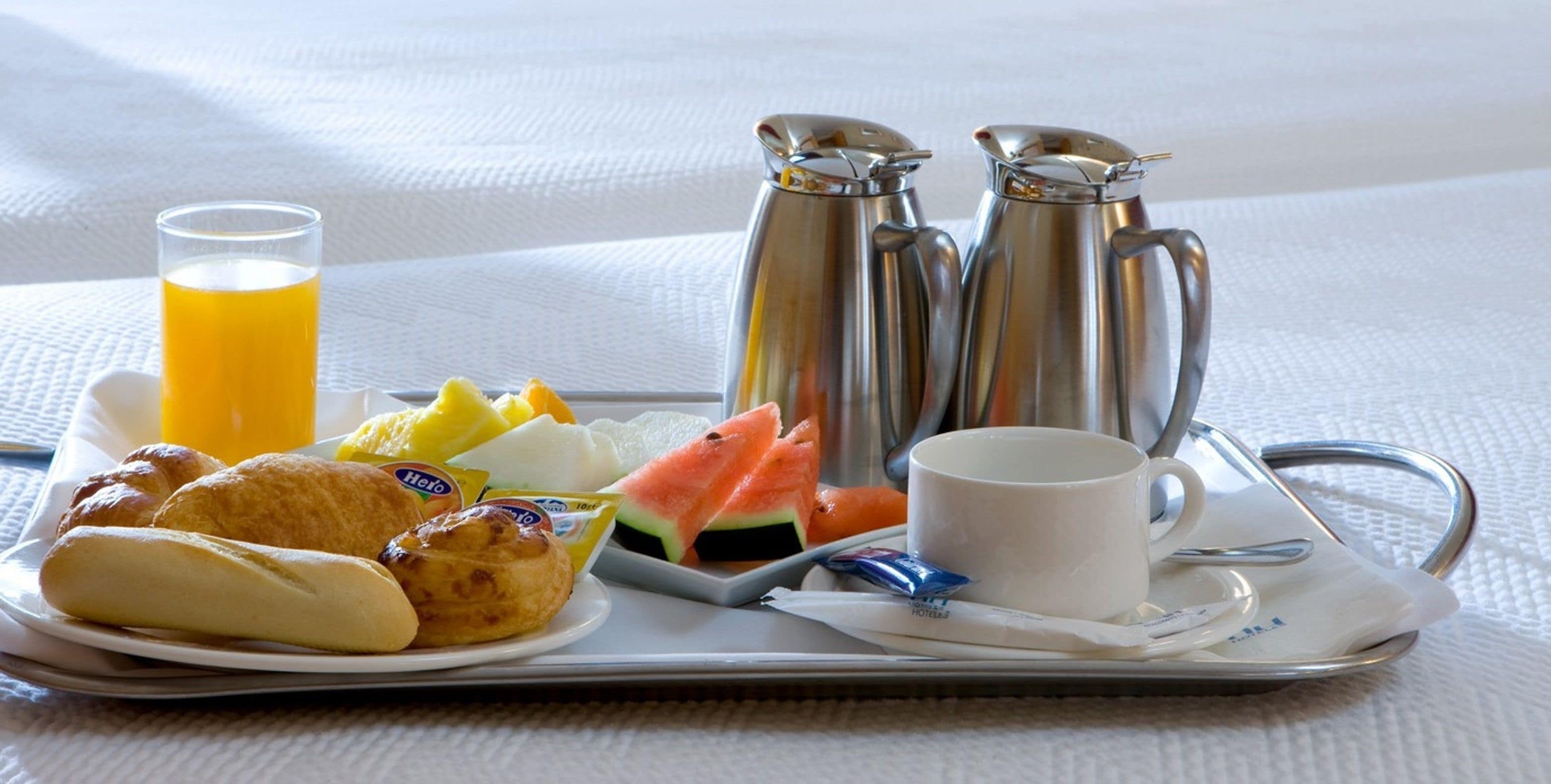 A tray with croissants, a glass of orange juice, a cup of coffee, a plate of fruit, and two silver coffee pots.