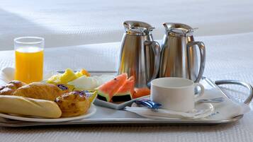 A tray with croissants, a glass of orange juice, a cup of coffee, a plate of fruit, and two silver coffee pots.
