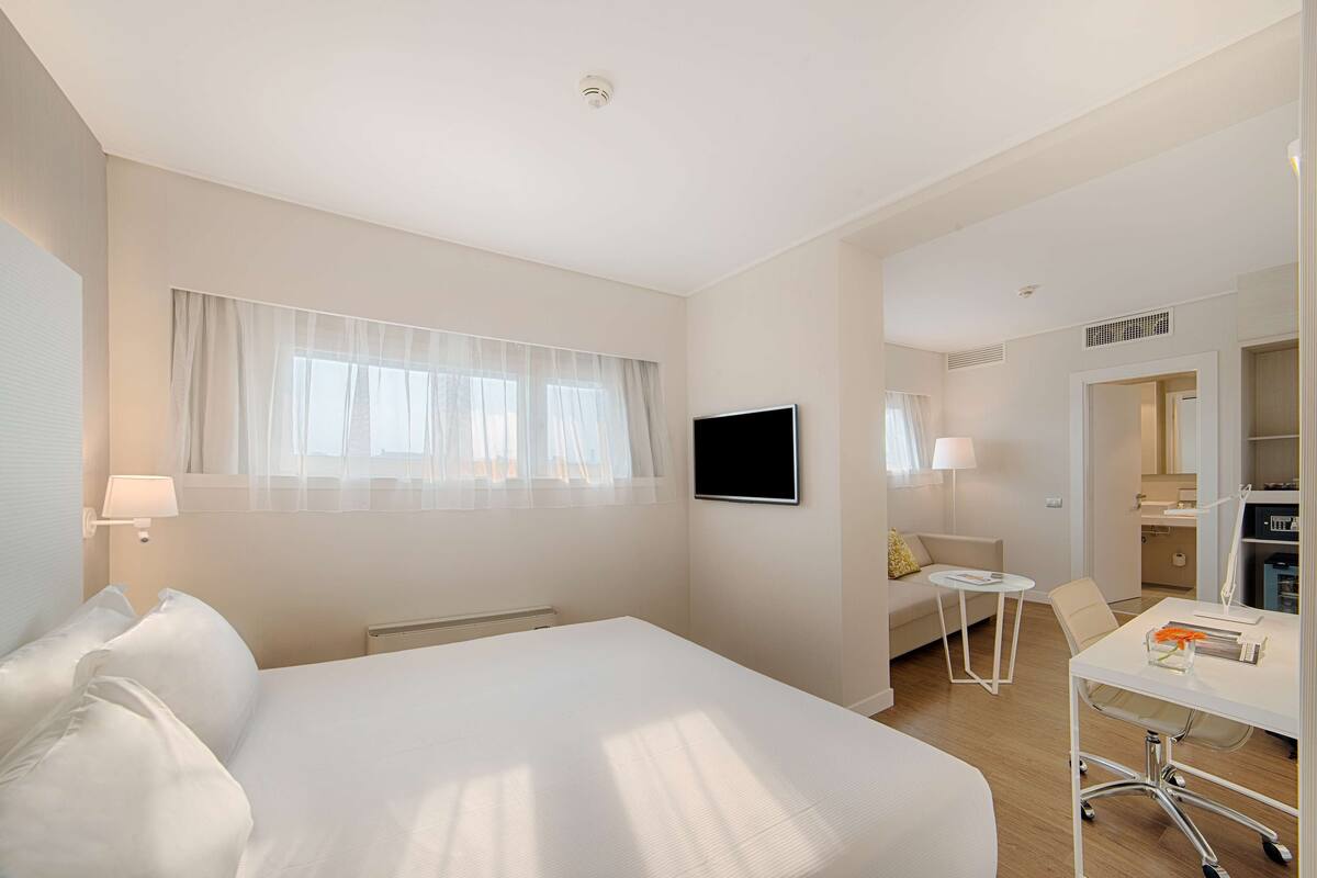A hotel room with a large bed, a TV, a desk with a chair, and a small table.