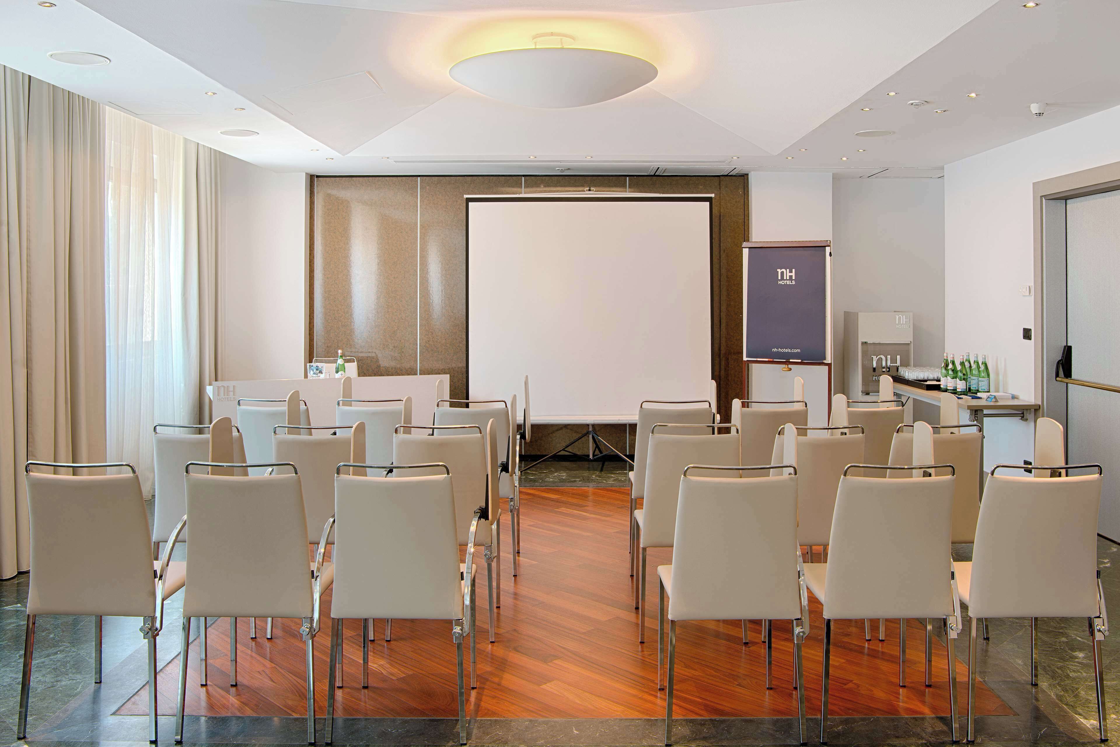 Una sala de conferències amb cadires blanques disposades en files, una pantalla de projector i una pantalla de presentació.