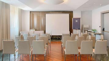 Una sala de conferències amb cadires blanques disposades en files, una pantalla de projector i una pantalla de presentació.