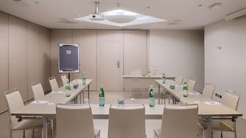 Un salón de conferencias con una larga mesa, sillas, una pantalla de proyector y botellas de agua.