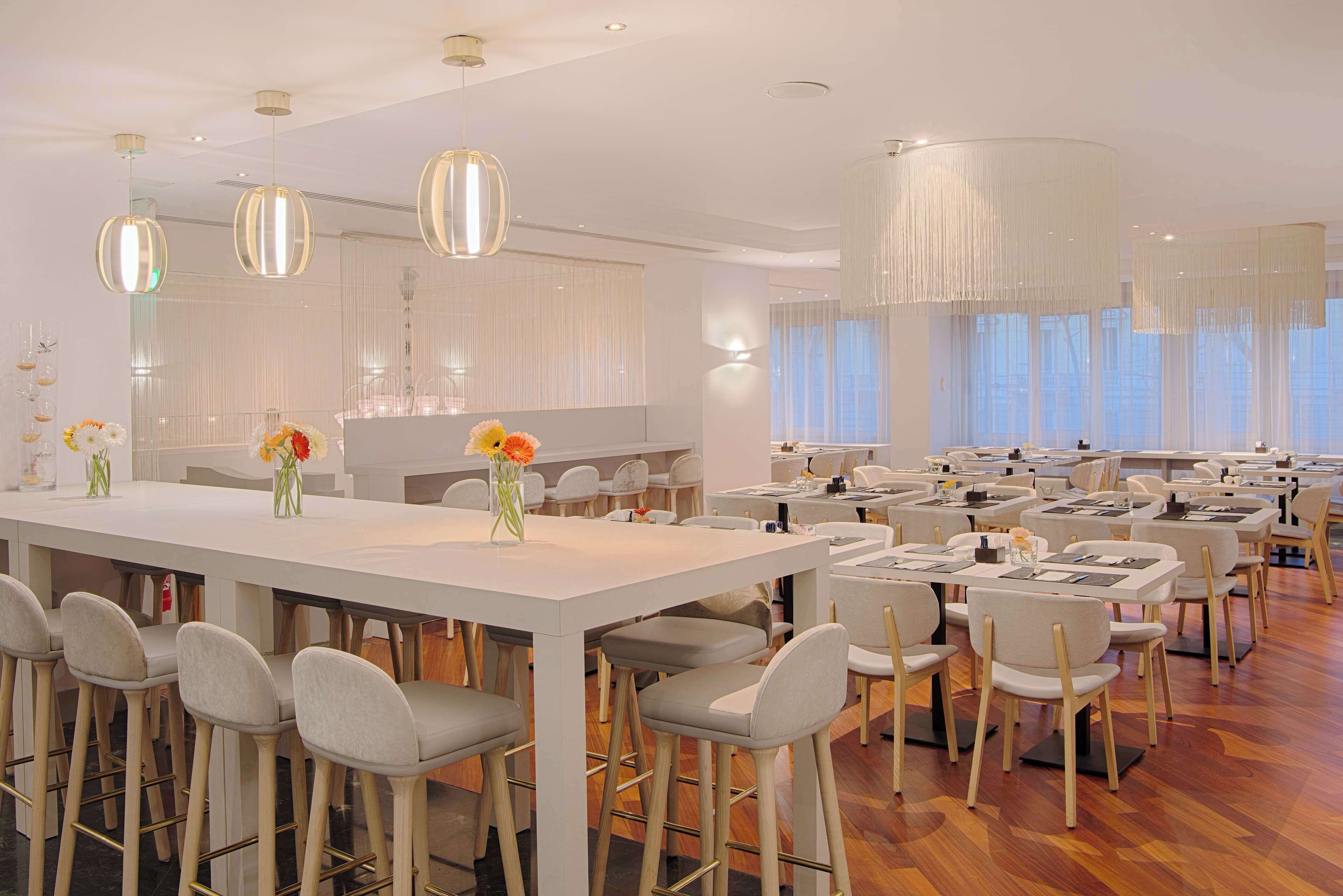 Un comedor amplio con varias mesas y sillas, una isla central con barra e iluminación colgante.