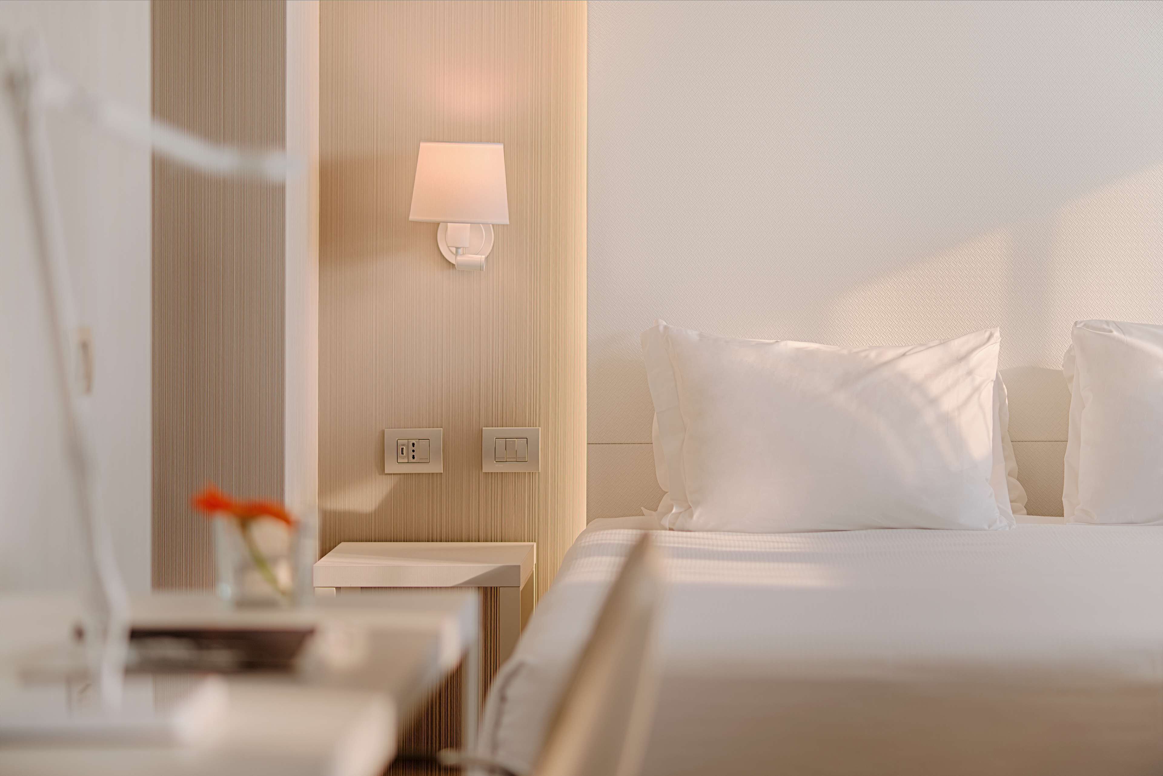 A hotel room with a bed, a bedside table, a lamp, and a wall-mounted light fixture.
