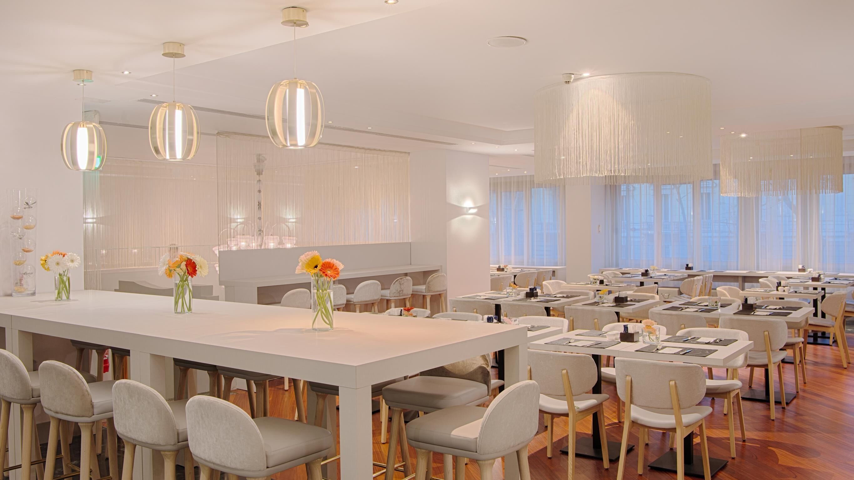 A modern dining area with a long table, multiple chairs, and hanging pendant lights.