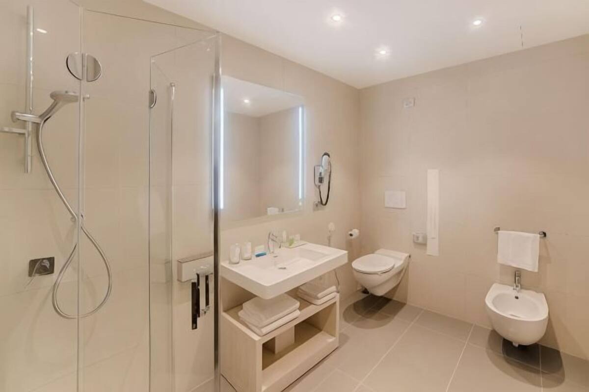 A modern bathroom with a glass shower enclosure, a sink, a bidet, and a toilet.