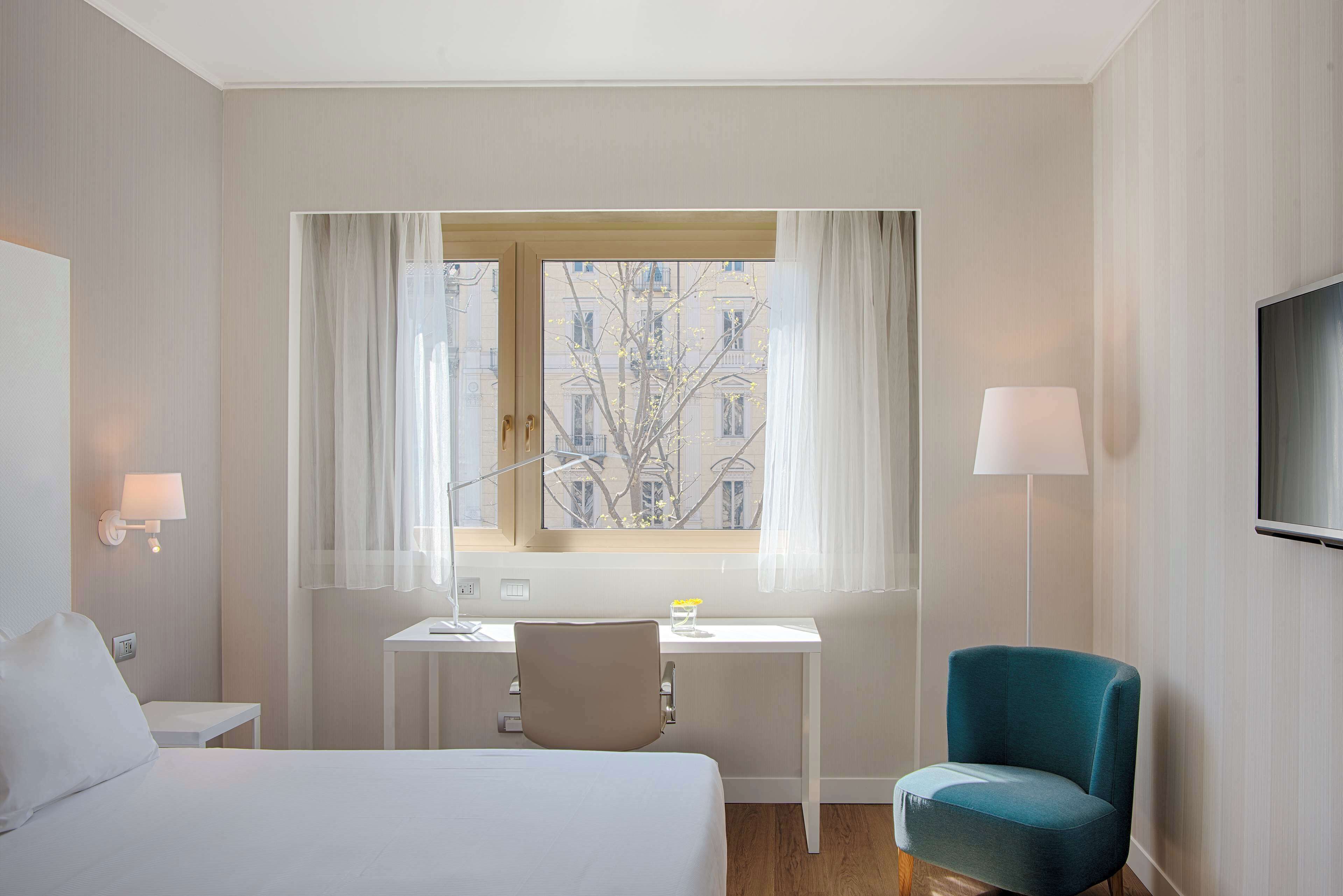 A hotel room with a bed, desk, chair, and a TV on the wall.