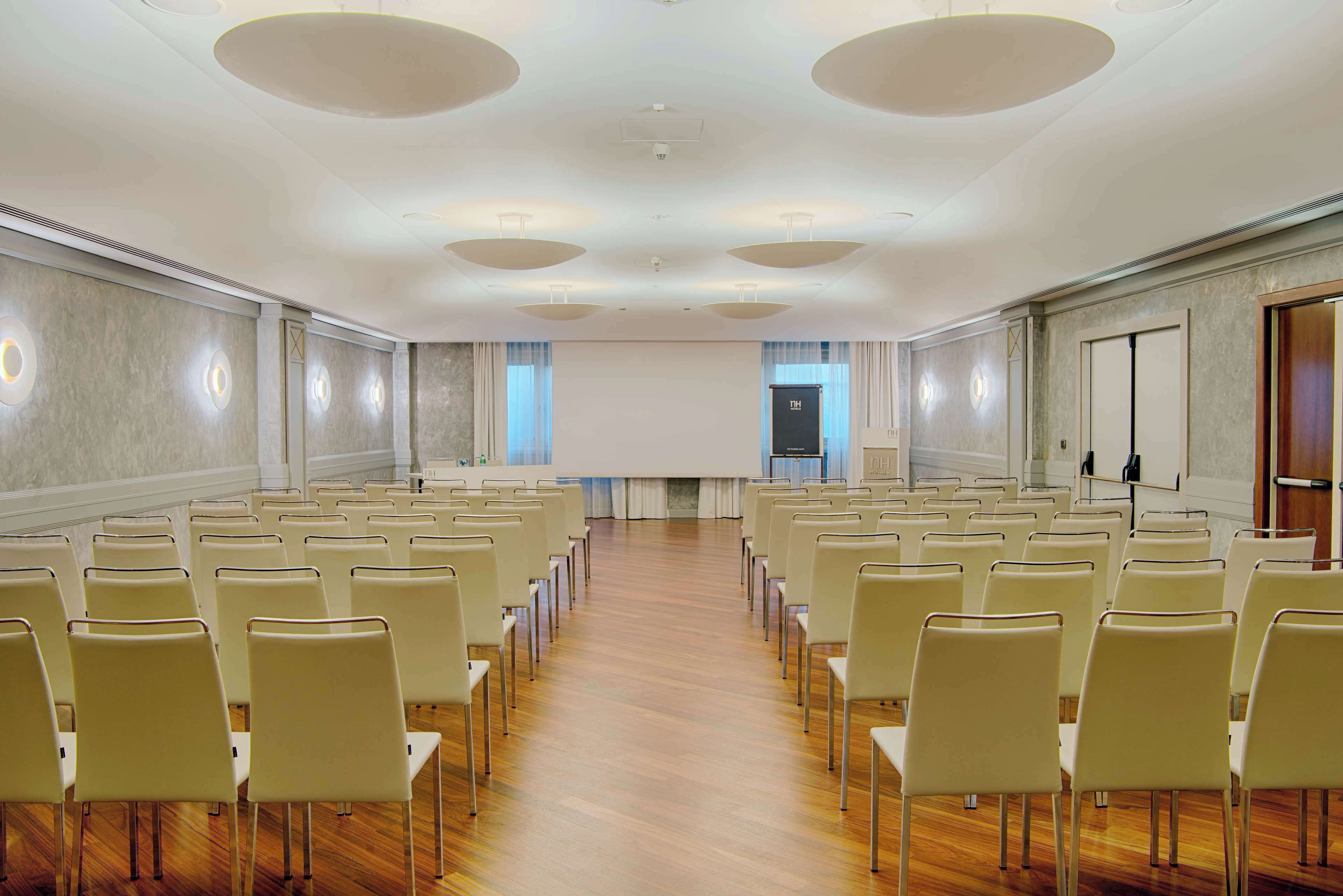 A conference room with rows of chairs, a projector screen, and a presentation area.
