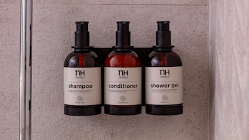 Three bottles of hotel toiletries (shampoo, conditioner, shower gel) on a wall.