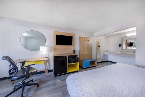 Habitación de hotel con cama, escritorio con silla, televisor, microondas y un pequeño armario.