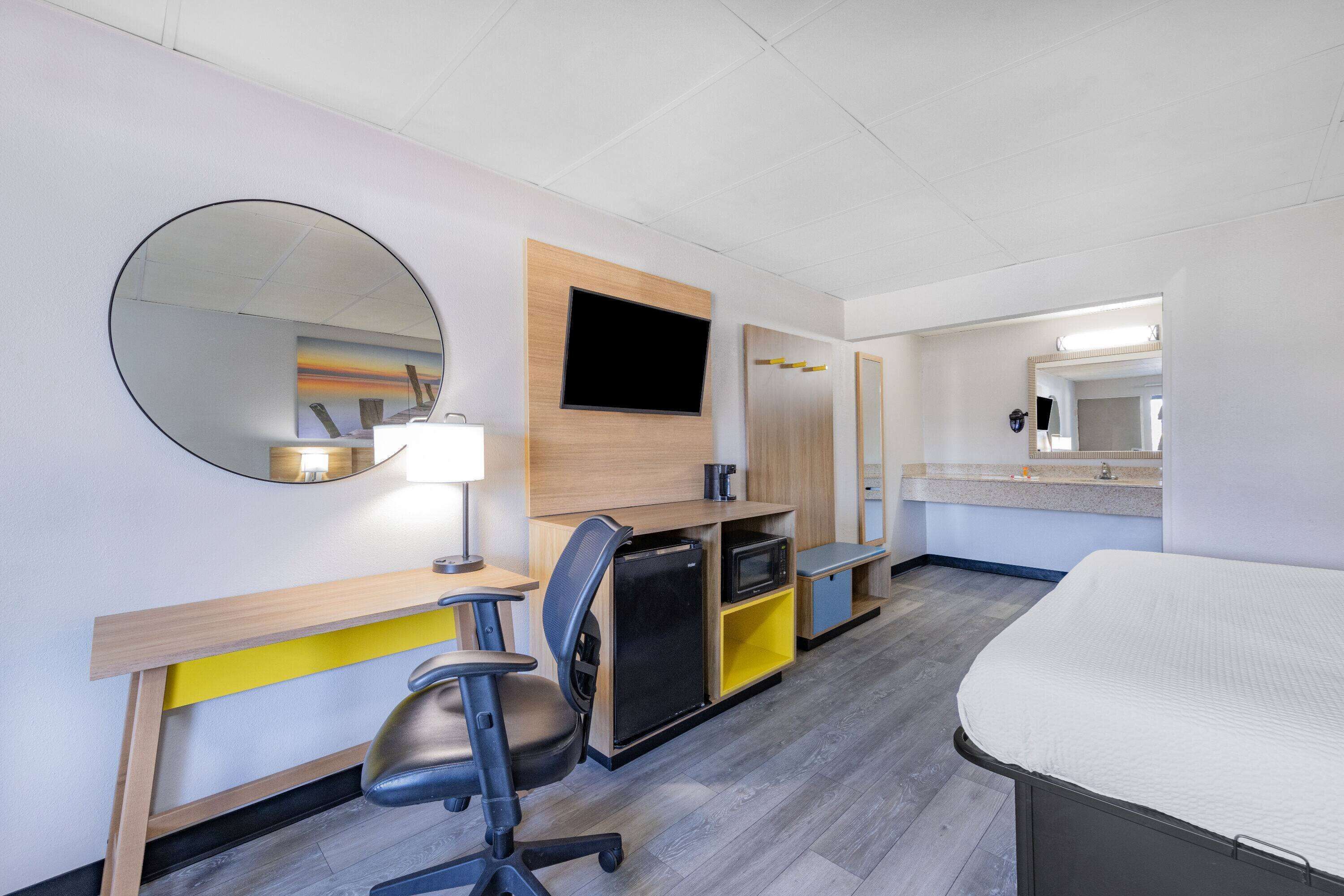Una habitación de hotel con cama, escritorio, silla, televisor, microondas y una pequeña cocina.