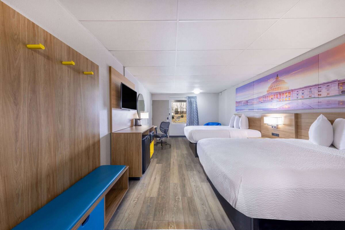 Ein Hotelzimmer mit einer Holzwand, einem Schreibtisch mit Stuhl, einem Bett und einem großen Wandgemälde eines Gebäudes.