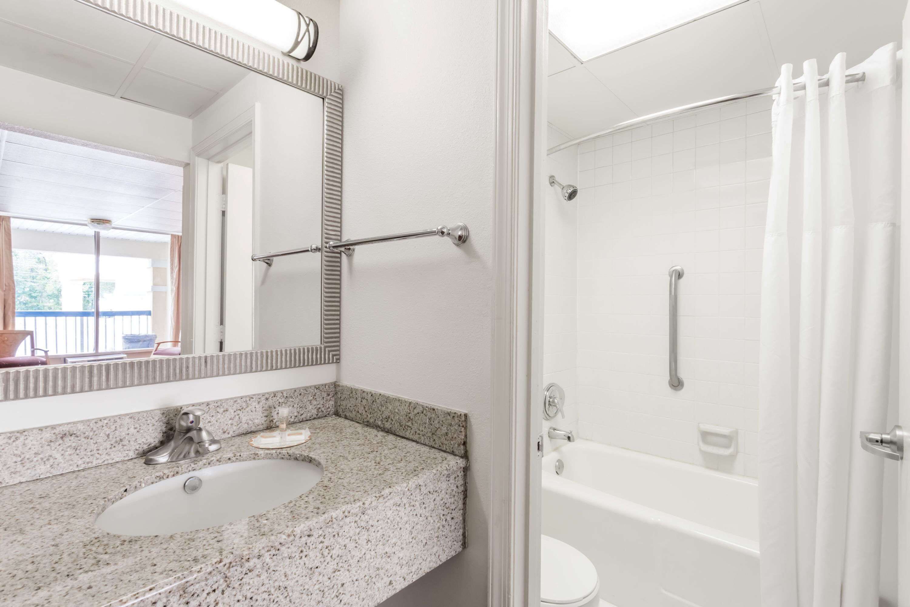 Een badkamer met een wastafel van graniet, een spiegel, een douche met glazen deur en een wit toilet.