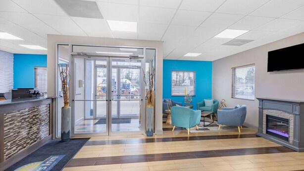 A reception area with a glass door entrance, a reception desk, and a seating area with two chairs and a fireplace. - Days Inn by Wyndham Fredericksburg North (Fredericksburg)