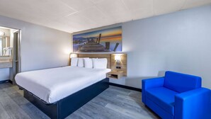 A hotel room with a bed, a blue sofa, a painting of a pier, and a nightstand with a lamp. - Days Inn by Wyndham Fredericksburg North (Fredericksburg)